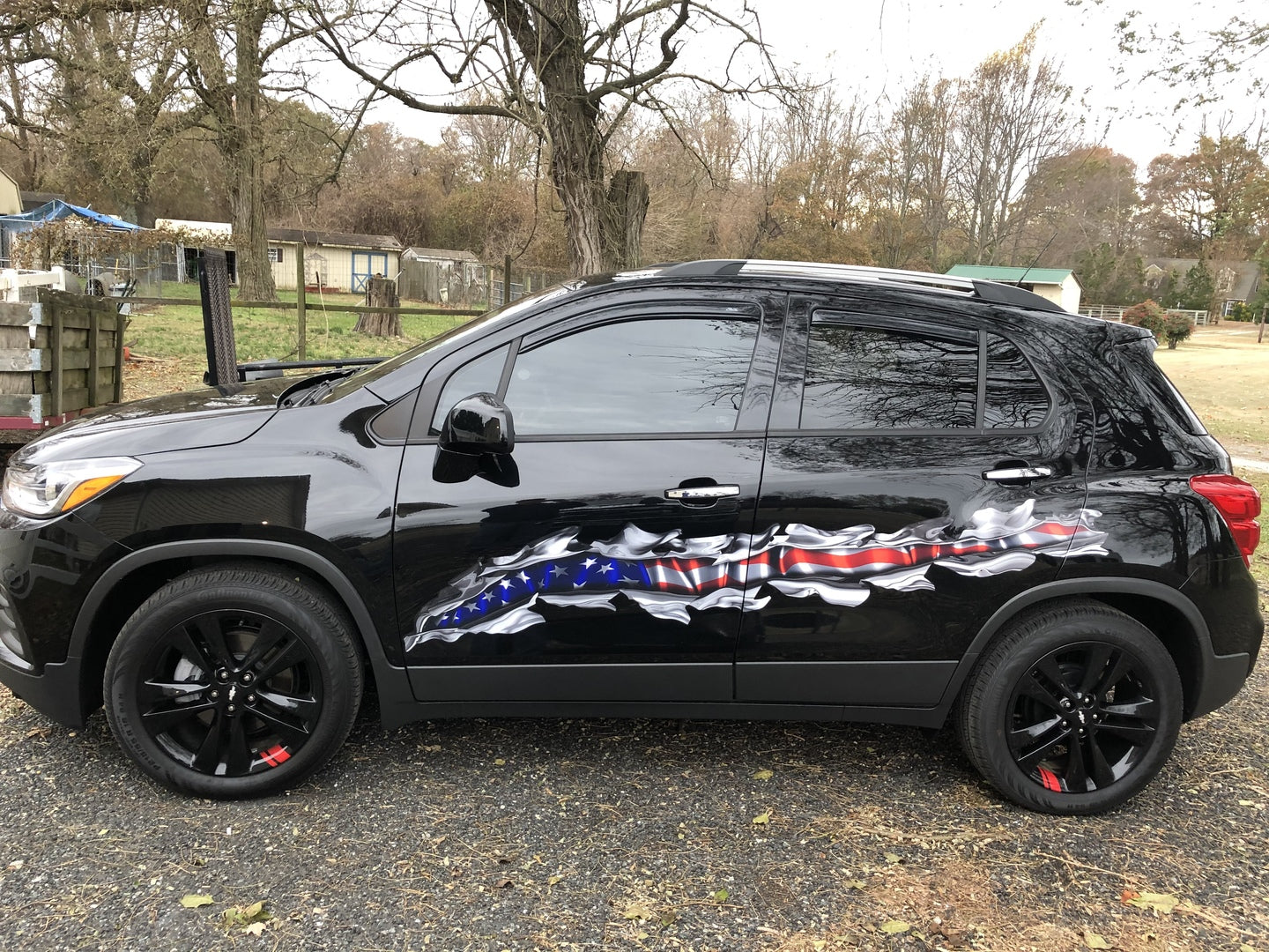 Driver side view of black Chevy SUV with chrome tear American flag vinyl decal across the doors