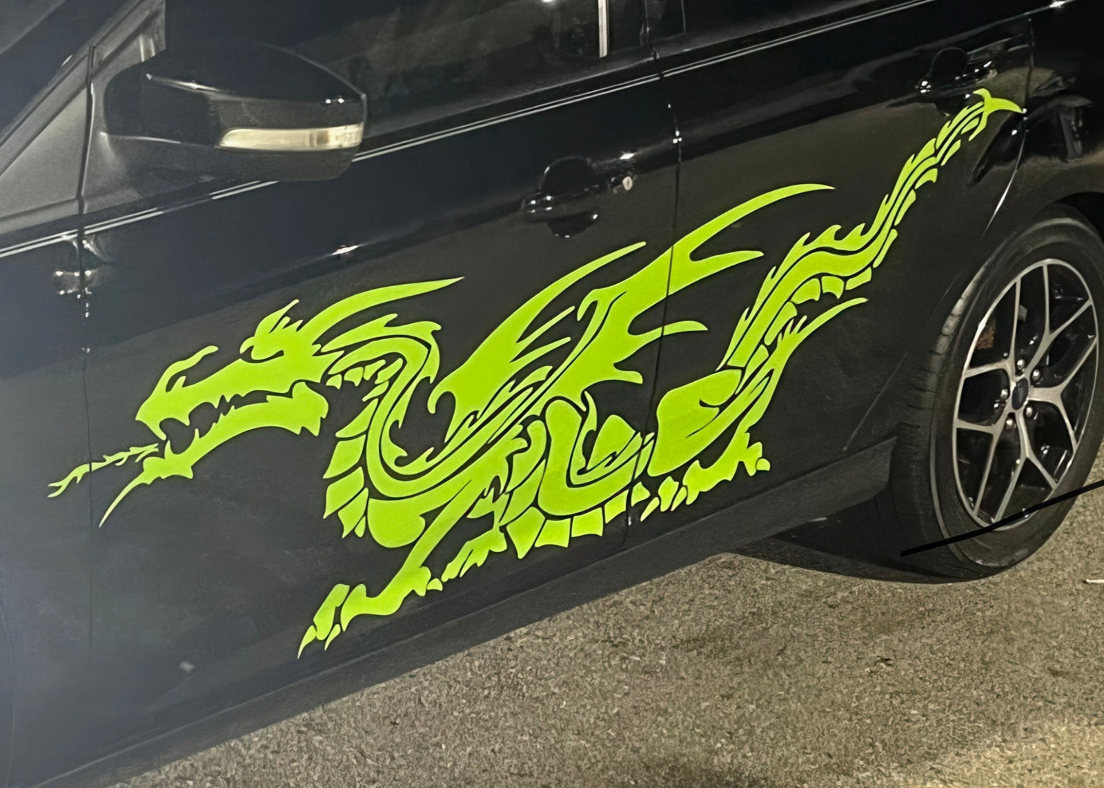Black car with a neon green western dragon decal on its side parked on street