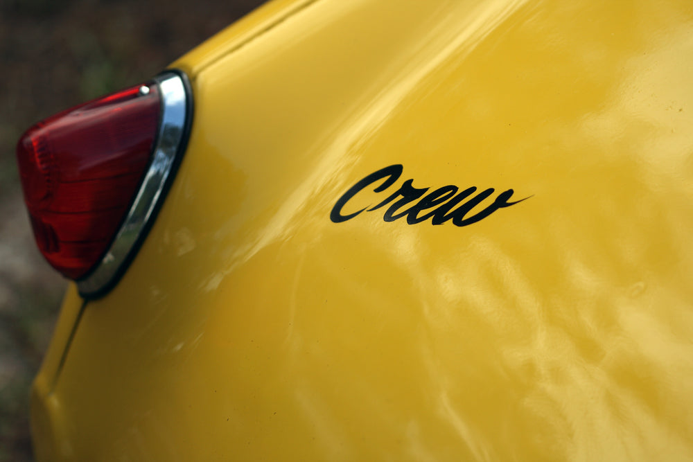 close up image of yellow car with red light and a black vinyl decal of the word "crew" 