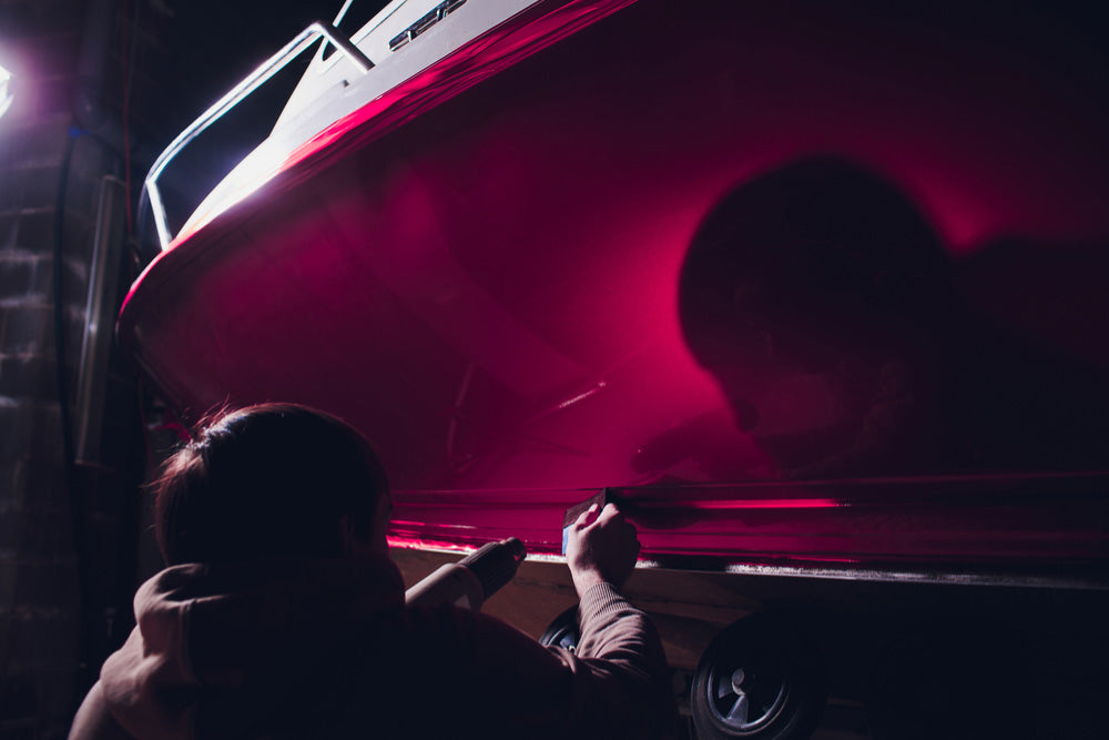 dark image of a person installing a red decal on a boat