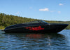 Black speedboat with a red tiger flame decal on a calm lake with trees in the background