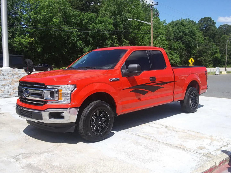 Red pickup truck with black vinyl stripe graphics parked on a paved surface with trees in the background.