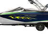 A speedboat on a dual-axle trailer, covered with a dark gray protective cover. The boat features a blue and white hull with green stripes, a yellow skulls flame graphic, and a wakeboard tower on top.