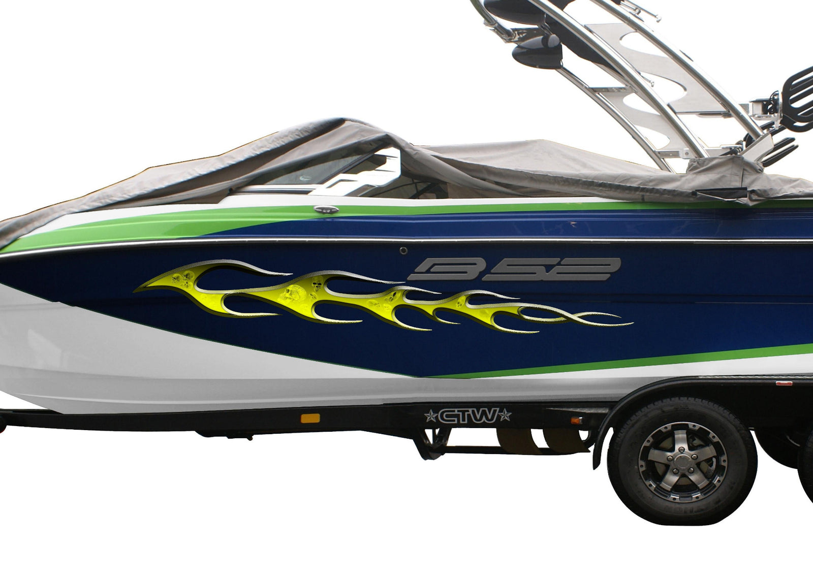 A speedboat on a dual-axle trailer, covered with a dark gray protective cover. The boat features a blue and white hull with green stripes, a yellow skulls flame graphic, and a wakeboard tower on top.