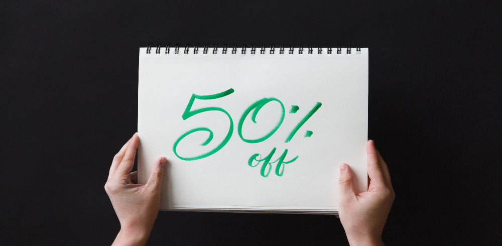 50% Off written on notebook held with two hands