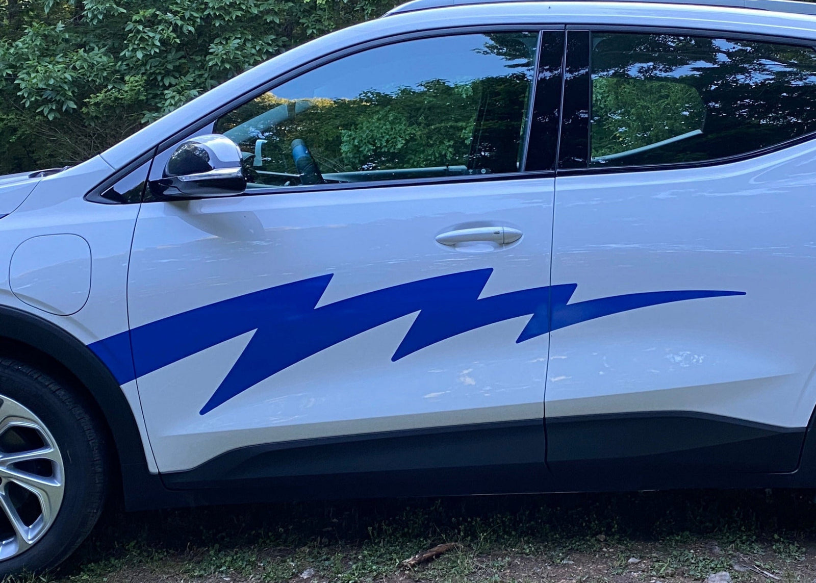 White SUV with blue lightning bolt decal parked on grass with trees in the background
