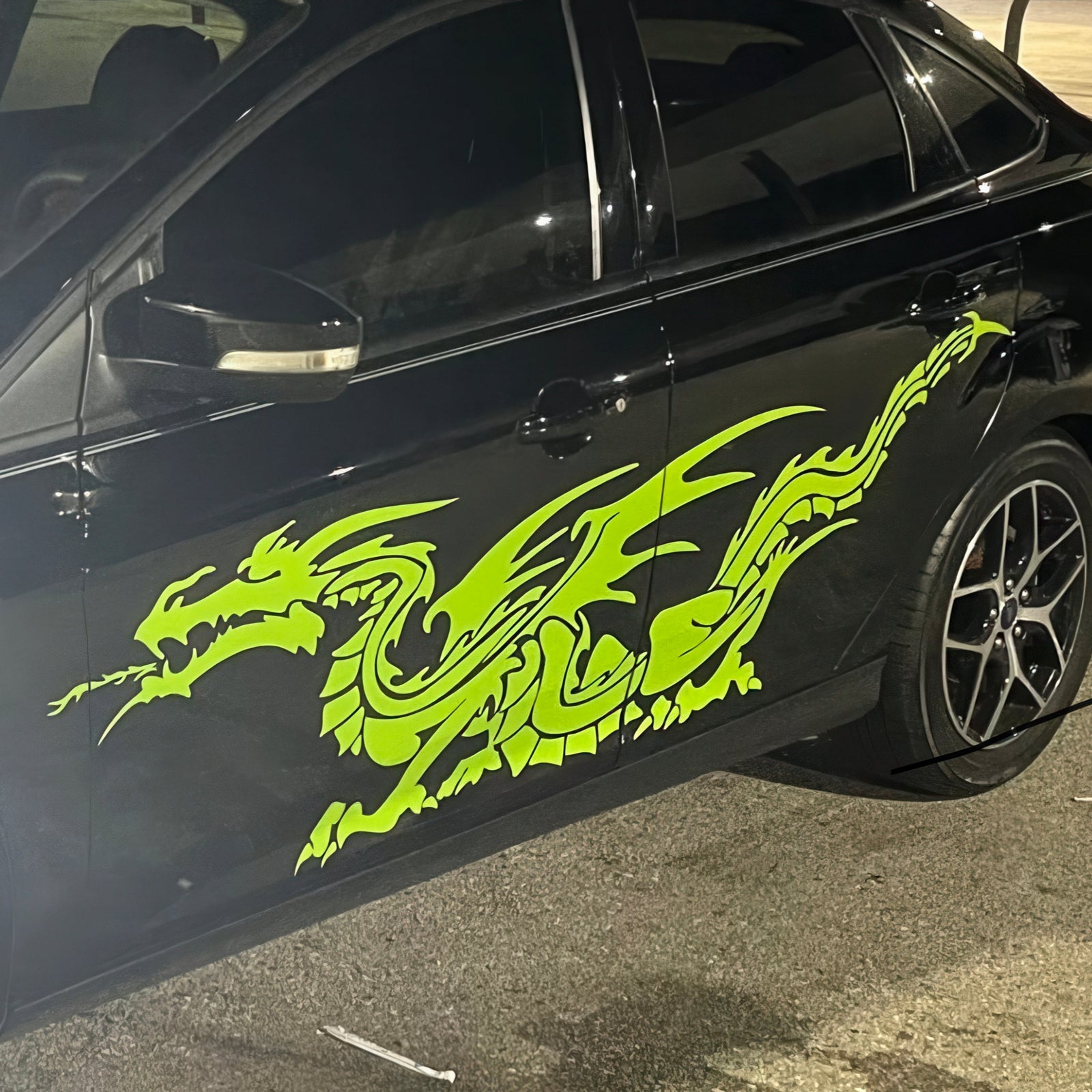 Black car with a neon green western dragon decal on its side parked on street