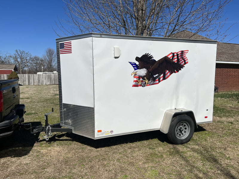 White small trailer with an eagle and American flag decal design parked on a grassy area.