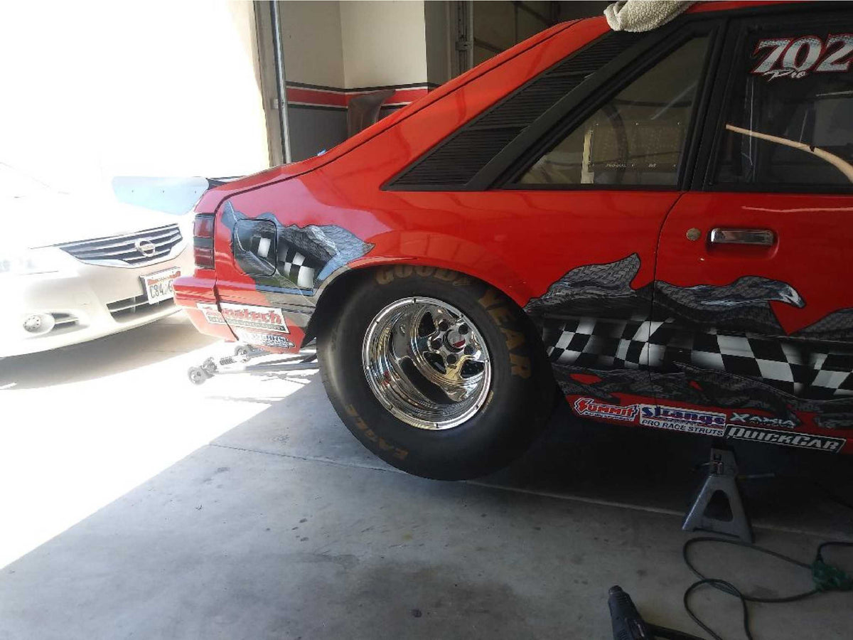red old style mustang with checkered flag carbon fiber rip on the back side, in mechanic shop lifted by jack.