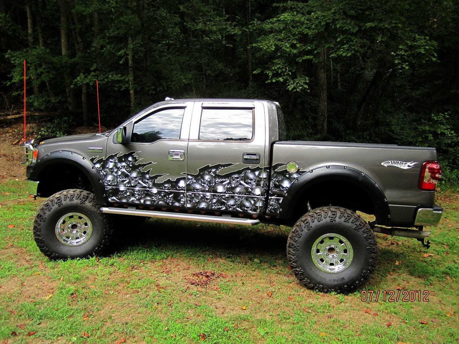 grey raised f150 pickup with gunmetal grey skulls and crossbones vinyl half wrap on driver side, parked on grass.